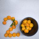 Mandarins carefully arranged on a bench to form a two. To make it twenty, a round container sits to one side containing more mandarins.