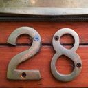 Brass house numbers two and eight screwed to wood with four screws, three rusted.