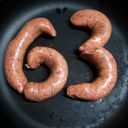 Four sausages in a cast iron frying pan. They are curved into meaty raw digits, forming a six and a three.