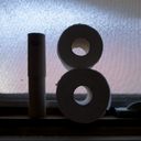 Two stacked toilet roll centers form the digit one alongside two whole rolls staked to form eight. Both silhouetted against a ripple glass window.